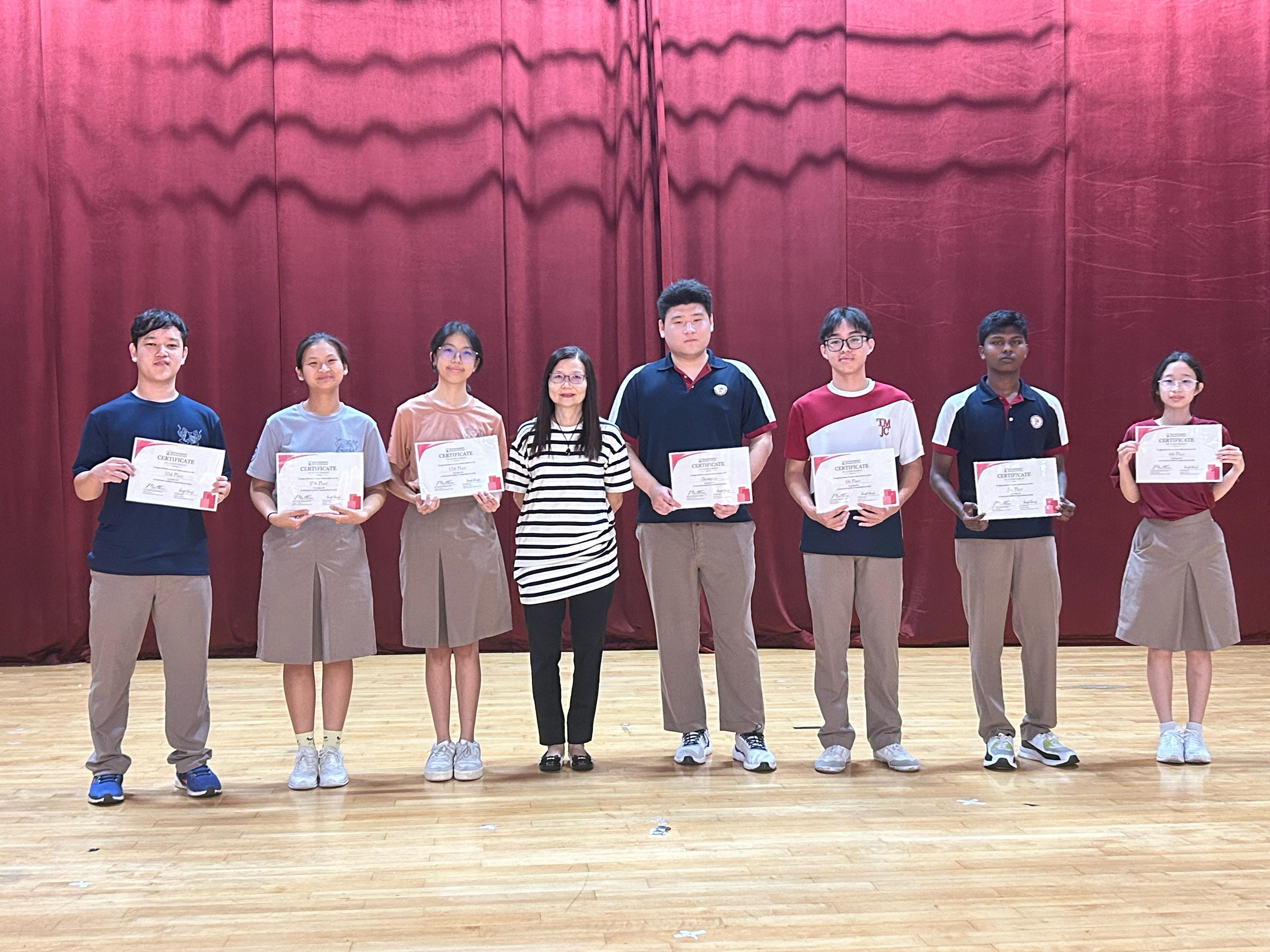 Eight people — seven students and one teacher — stand in a line on a stage in front of a red curtain, each holding a certificate. The students are in a mix of school uniforms and casual attire, representing their achievement at the National Cashflow Competition 2025.